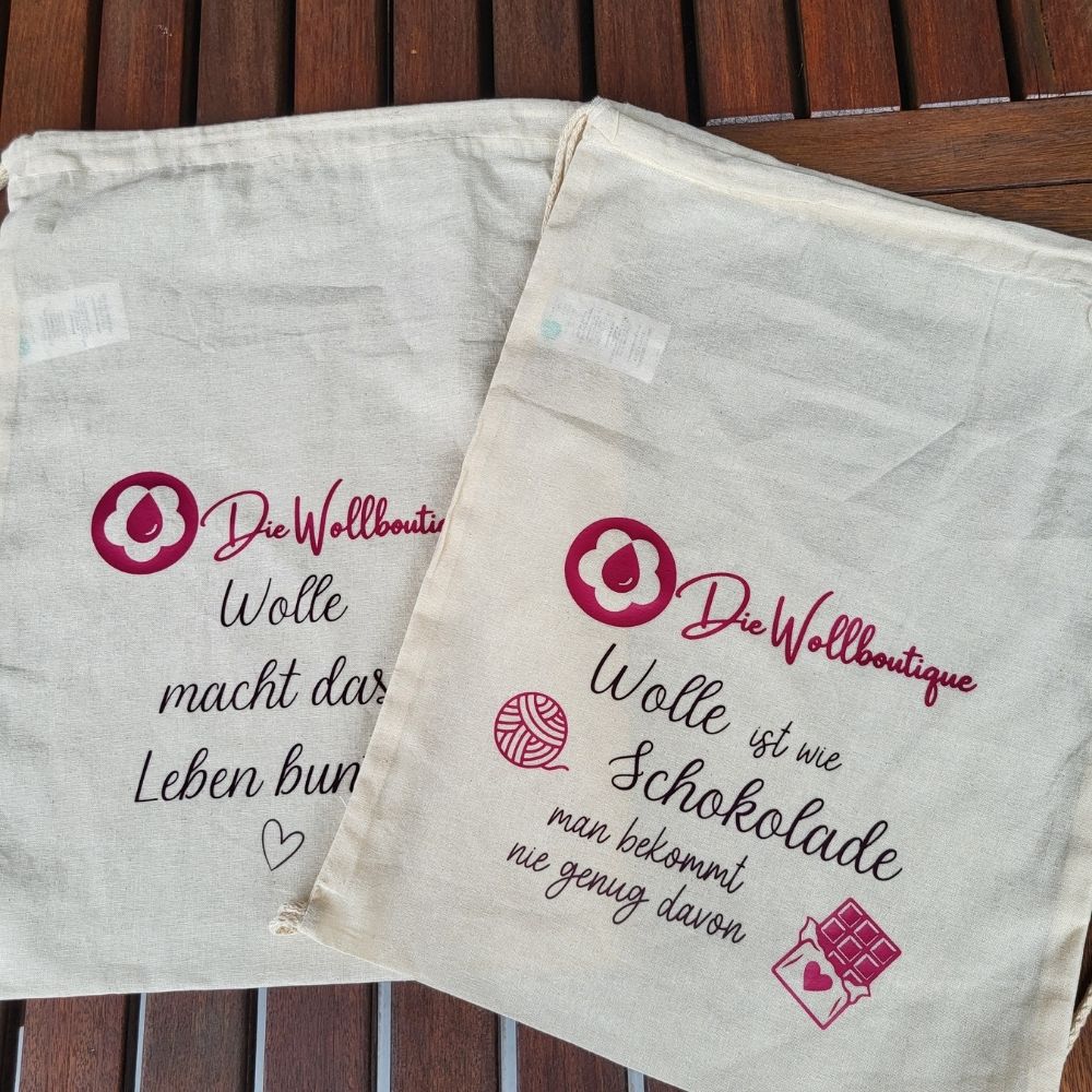 Zwei Baumwolltaschen der Wollboutique mit den Sprüchen “Wolle macht das Leben bunt” und “Wolle ist wie Schokolade”